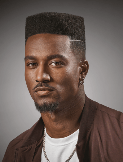 Man with a high top fade haircut dressed in brown jacket looking at camera