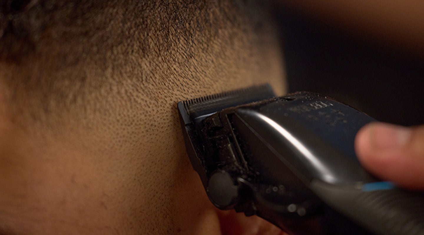 A close-up of a hair clipper trimming hair on the side of a person's head.