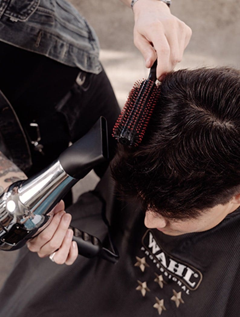 Barber styling a model's hair with a brush and a Wahl Barber Dryer.