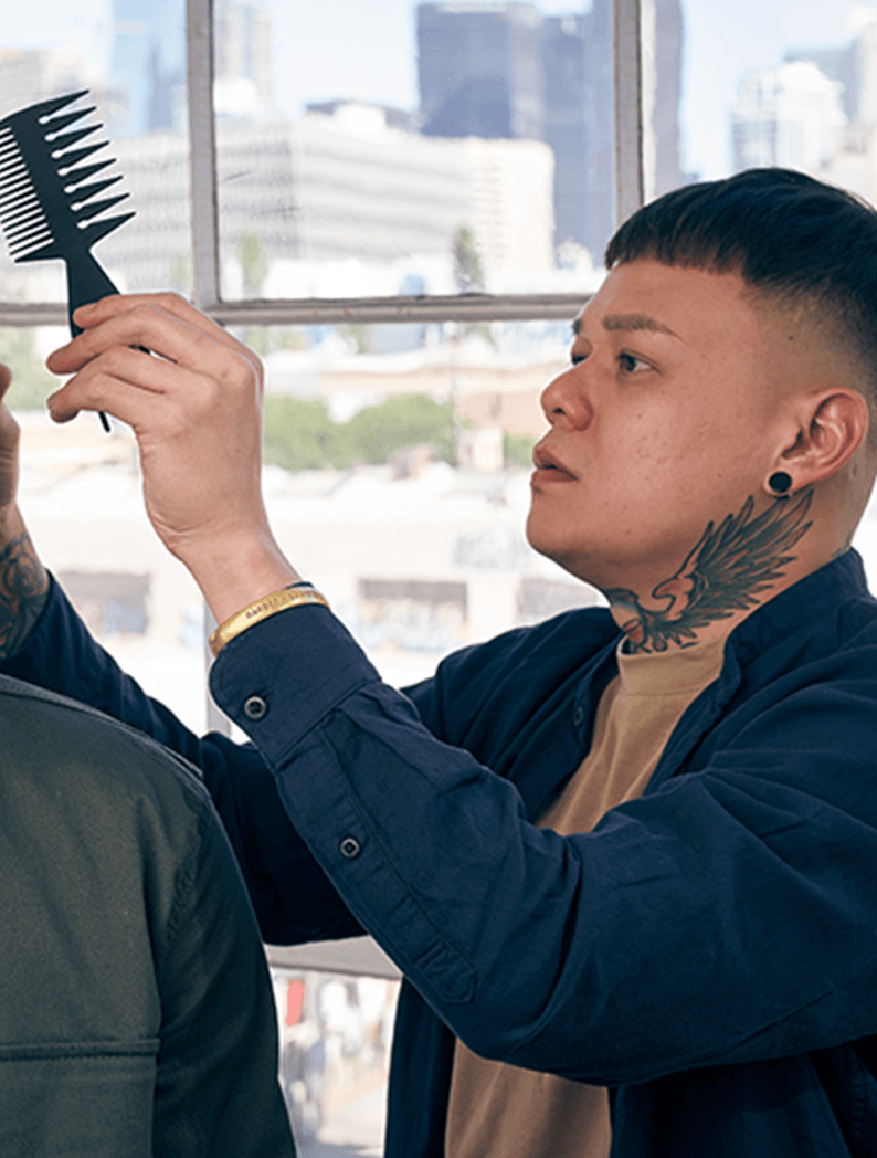 Male barber with a tattoo on his neck dressed in a dark blue shirt holding a comb