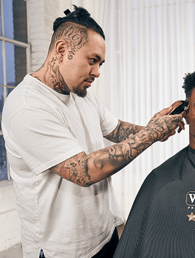 Male barber with tattoos dressed in a white t-shirt holding a clipper