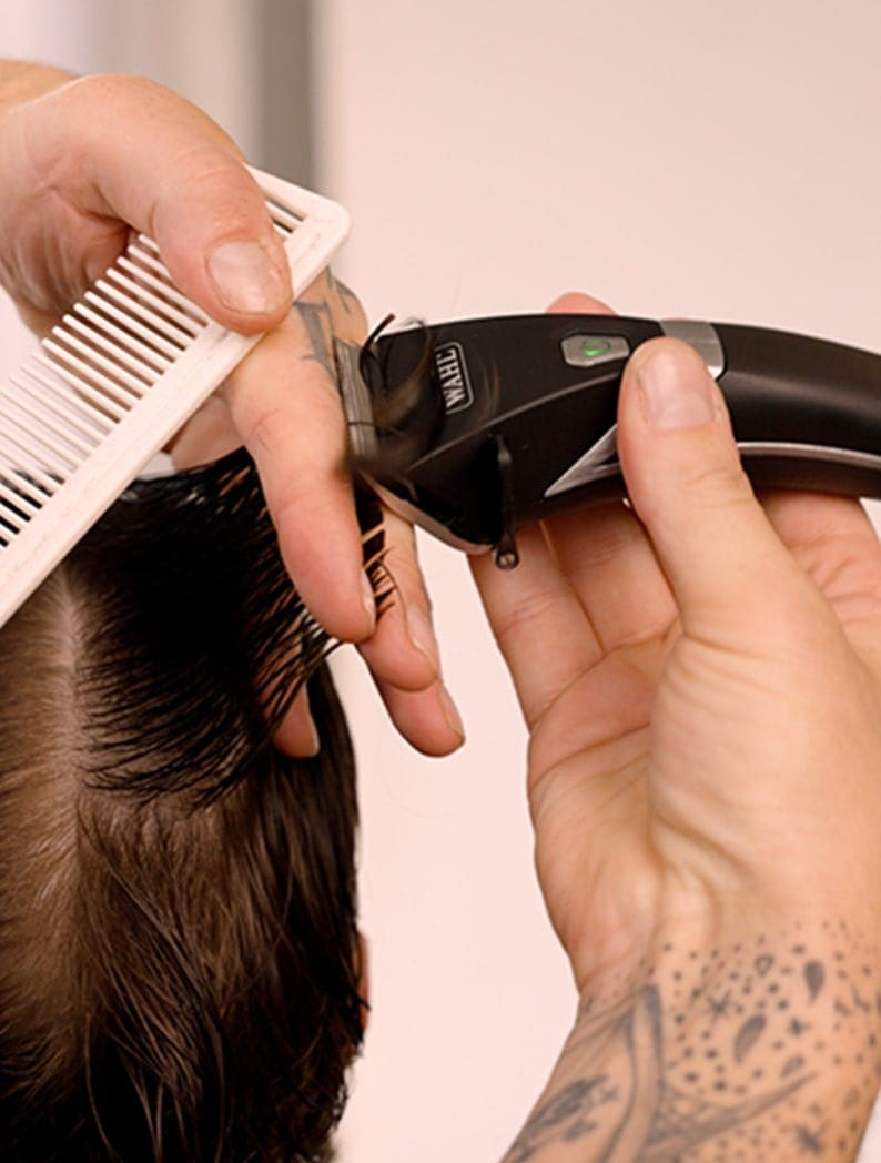 Barber using Wahl clipper to style model's hair.