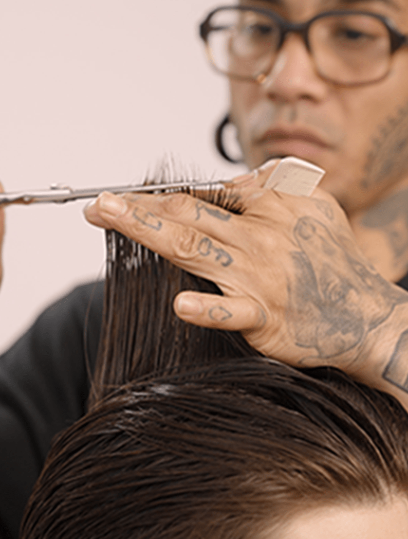 Barber with glasses cutting hair with scissors and a comb